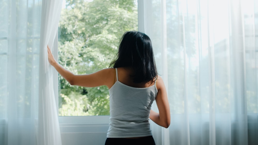 happy-beautiful-asian-woman-smiling-drinking-cup-coffee-tea-near-window-bedroom-young-latin-girl-open-curtains-relax-morning-lifestyle-lady-home-1-min